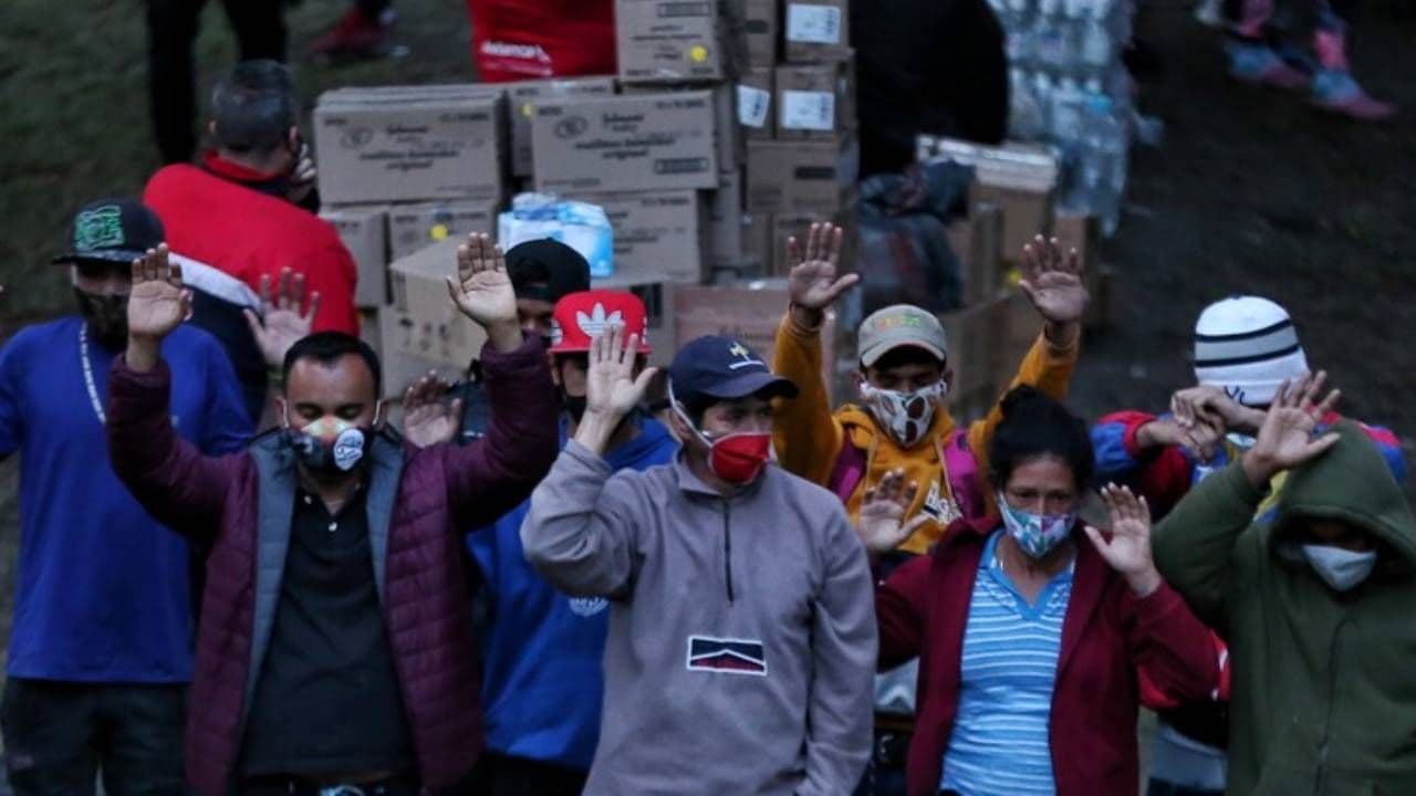 Población migrante en Colombia levantando las manos mientras se encuentra reunida en un parque.